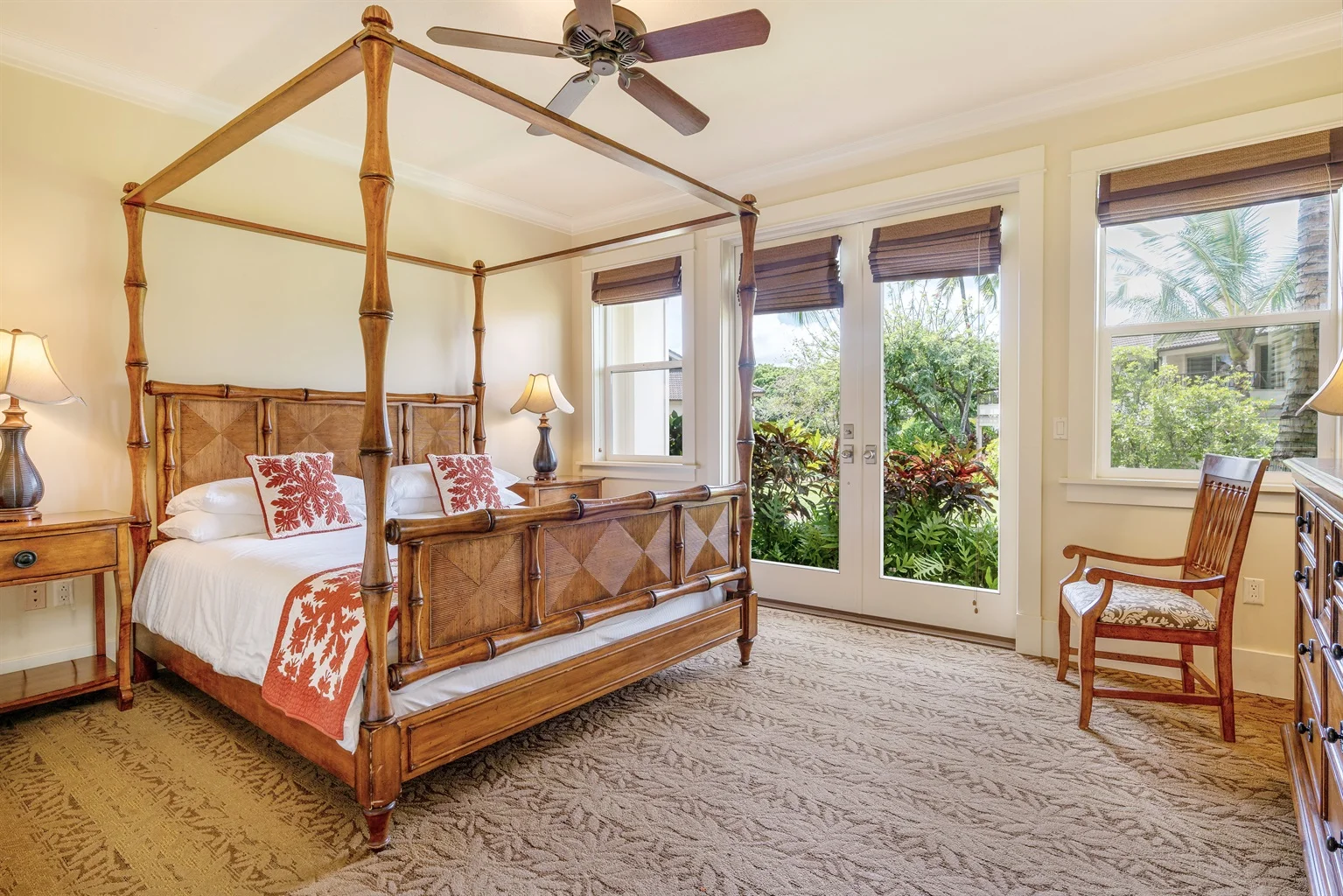 King bedroom featuring a four-poster bed with tropical decor, bedside lamps, and large windows opening to a lush garden view, embodying luxury and comfort for vacation rentals in Kauai.