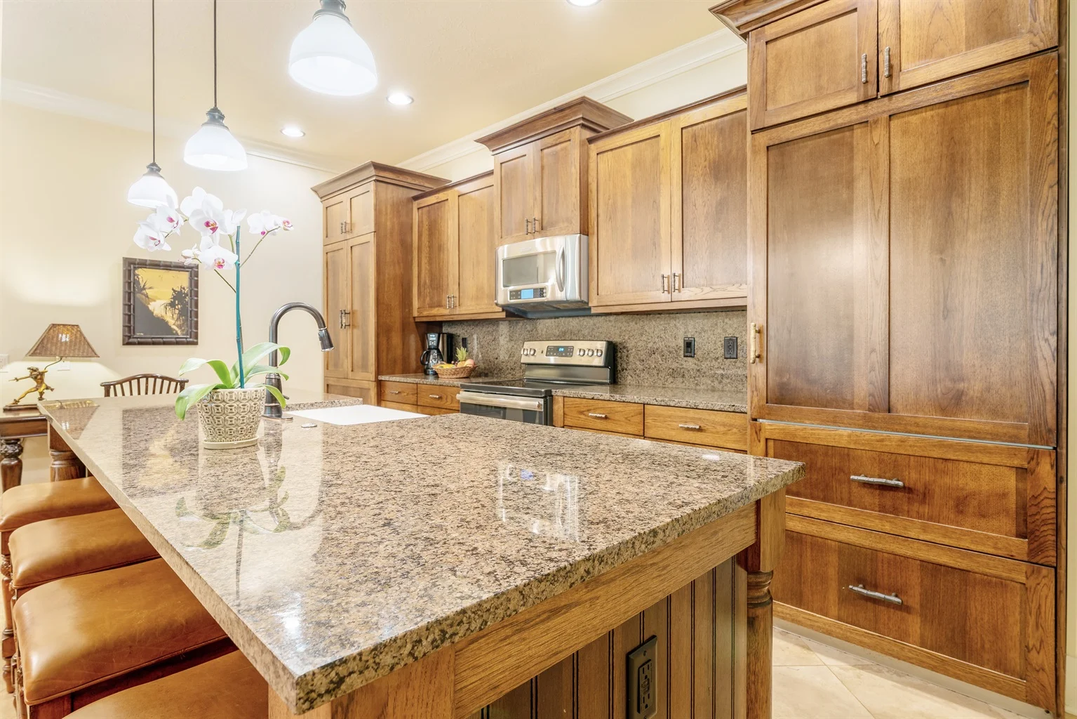 Modern kitchen with granite countertop, wooden cabinets, stainless steel appliances, and decorative orchid plant, reflecting luxury vacation rental amenities in Kauai.