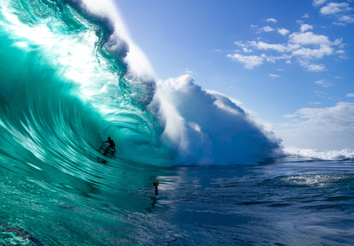 Surfer riding a large, vibrant wave in clear blue ocean waters, showcasing the thrilling ocean adventures available in Kauai.