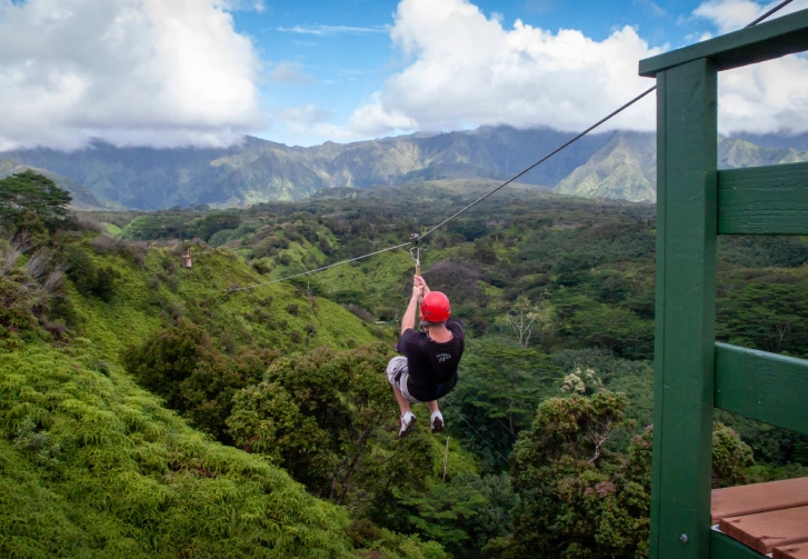 Person ziplining over lush green mountains in Kauai, showcasing adventure activities available on the island.
